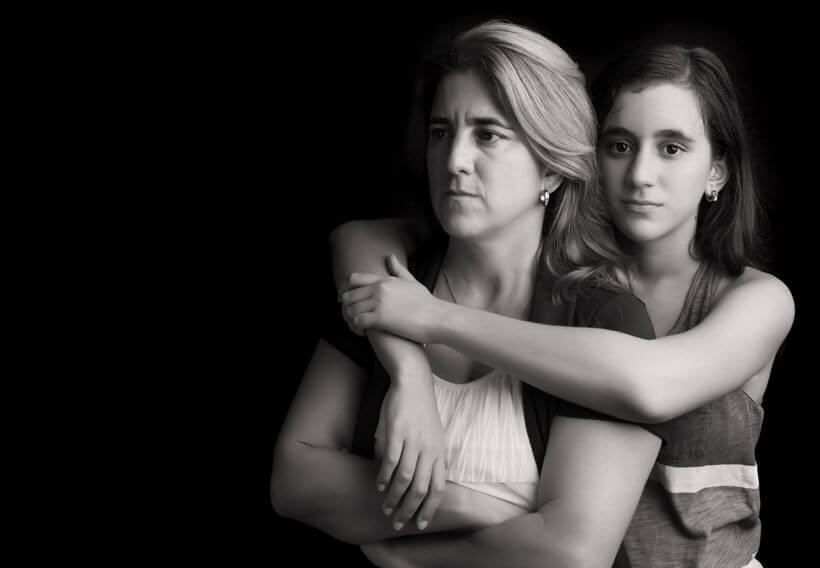 Emotional black and white portrait of a sad and angry mother with her teen daughter embracing her
